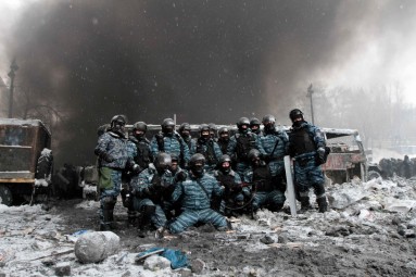 Riot police officers pose for a picture near burnt vehicles as smoke rises in the background during clashes with pro-European protesters in Kiev